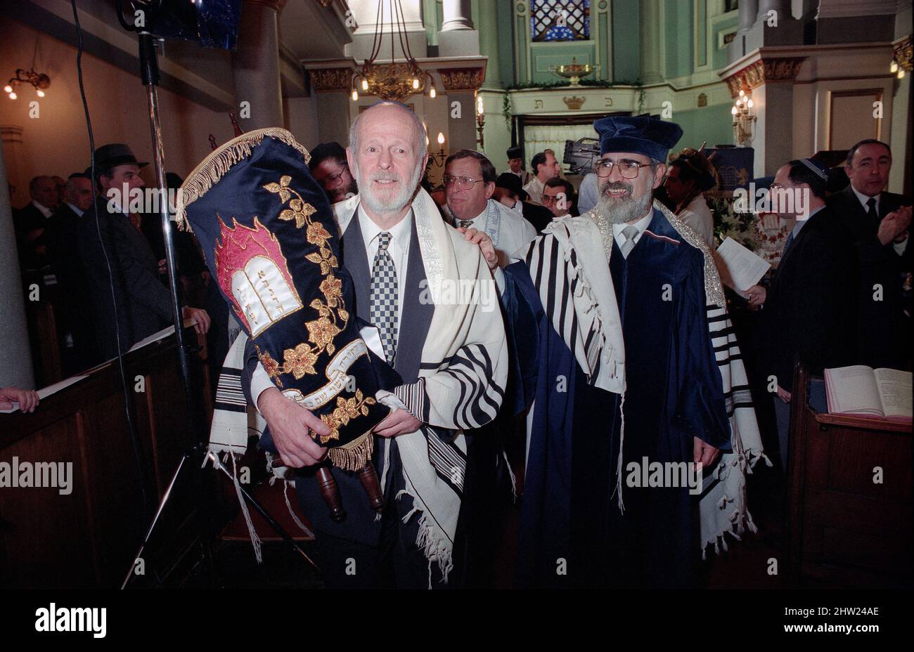 Die neue Sefer Tora wird um die Synagoge getragen, damit die Gemeinde ihre Achtung zollt. Der Oberrabbiner Jonathan Sacks war Ehrengast für die Aufnahme der letzten Briefe in eine neue Sefer-Torah in der Synagoge der hebräischen Kongregation Singers Hill am Sonntag, dem 15. März 1998. Mitglieder der Gemeinde sowie der Oberrabbiner fügten jeweils einen einzigen Brief hinzu. Stockfoto