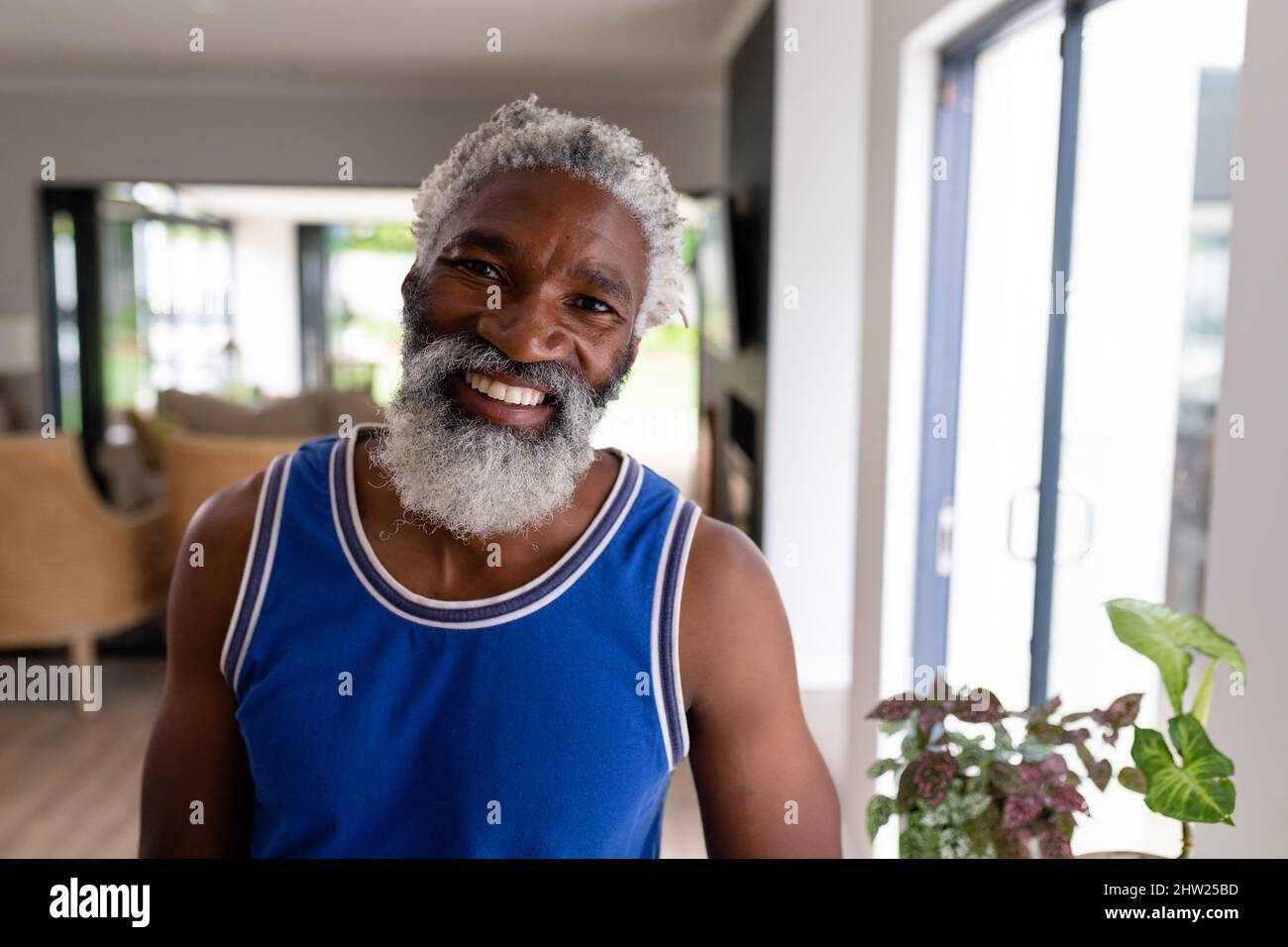 Porträt eines afroamerikanischen älteren Mannes mit weißem Bart und blauer Weste, der zu Hause lächelt Stockfoto