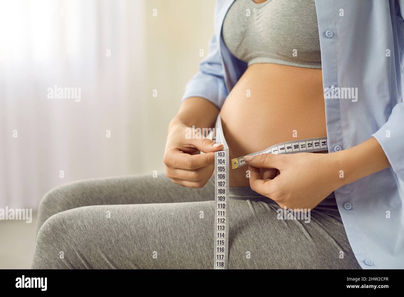 Eine glückliche, gesunde junge, schwanger Frau mit einem Maßband um ihren wachsenden Bauch Stockfoto