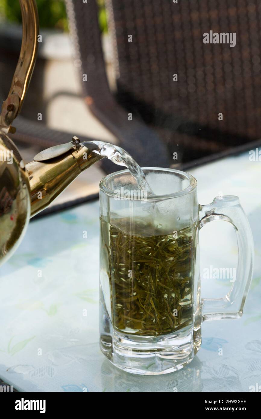 Frisch zubereiteter Aufguss von Chinatee mit kochendem Wasser, das aus einer Teekane mit heißem Wasser in dicke, geschnittene chinesische Teeblätter in Glasgläsern gegossen wird. Stadt Songpan im Norden von Sichuan, China. (125) Stockfoto