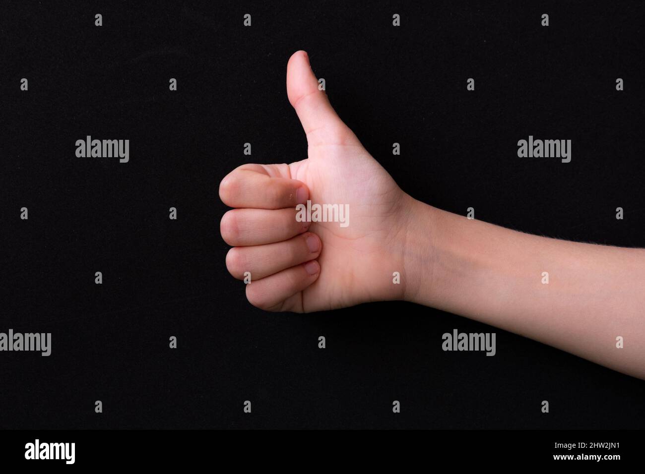 Nahaufnahme der weiblichen Hand, die den Daumen zeigt, auf schwarzem Hintergrund. Stockfoto