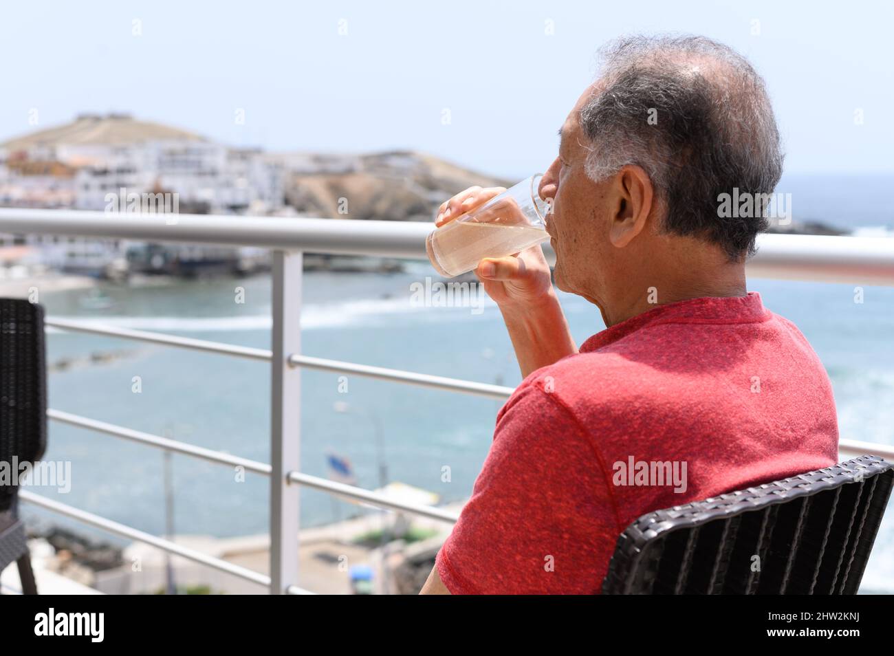 Reifer Mann, der auf einem Balkon mit Blick auf das Meer bei einem Cocktail sitzt Stockfoto