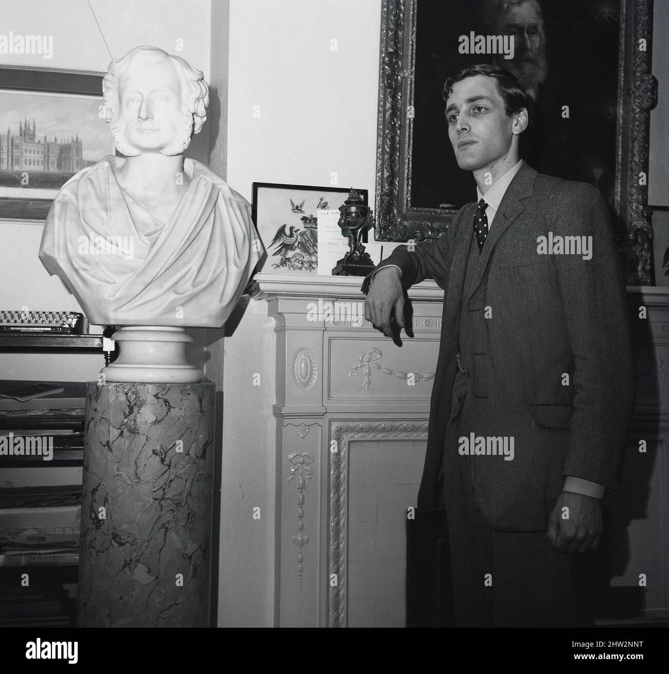 1960s, historical, Merlin Charles Sainthill Hanbury-Tracy, 7. Baron Sudeley, The Lord Sudeley steht neben einer Marmorbüste seines Vorfahren Charles Hanbury-Tracy, 4. Baron Sudeley. Der ehrenwerte Baron von 4., ein liberaler Politiker, war berühmt für sein gotisches Herrenhaus, das Toddington Manor, das teilweise als Vorbild für die Houses of Parliament gilt, als sie in den Jahren 1840s nach einem Brand erbaut wurden. Stockfoto