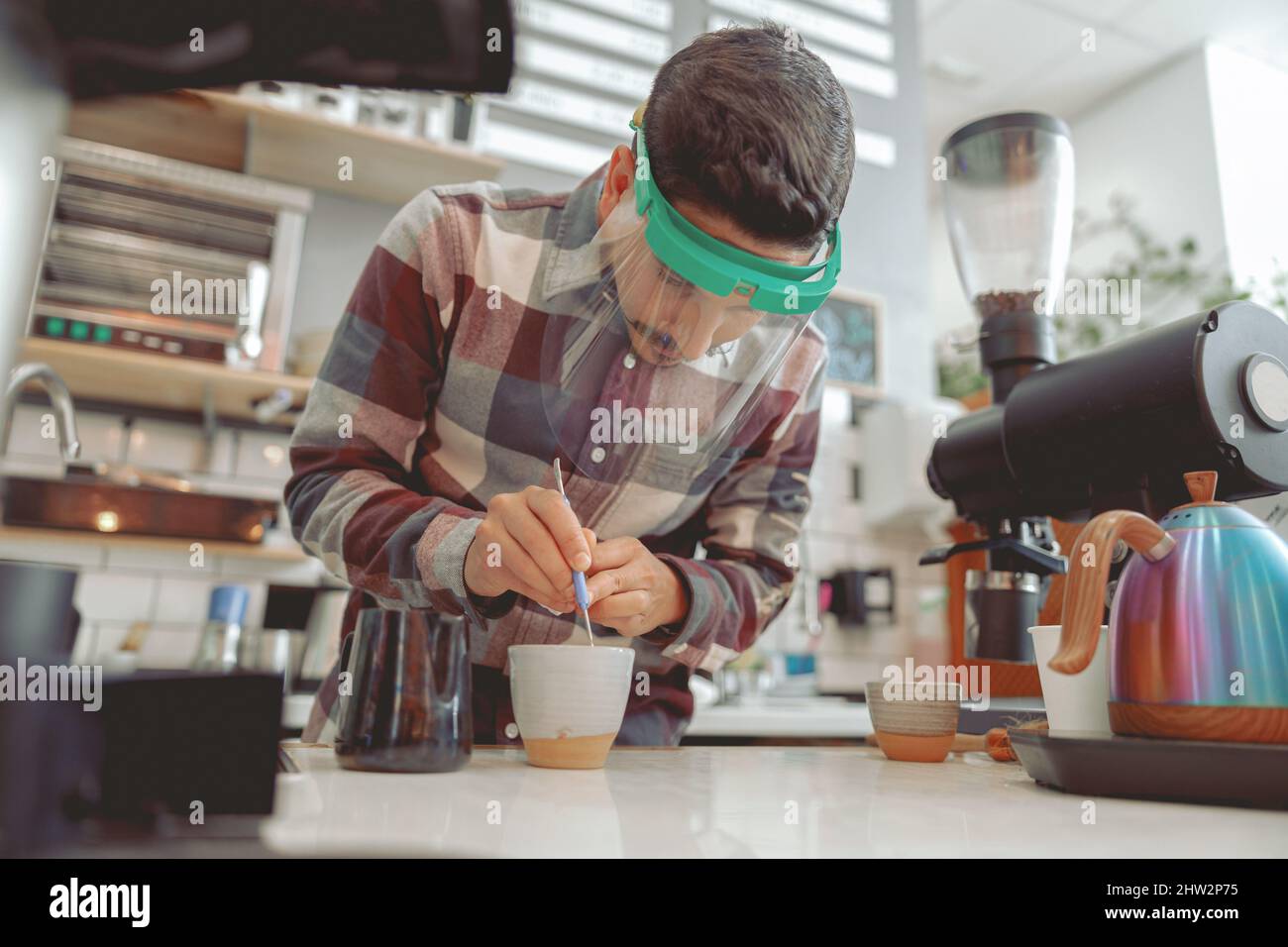 Barista mit Schutzvisier, der ein Muster auf dem Kaffee macht Stockfoto