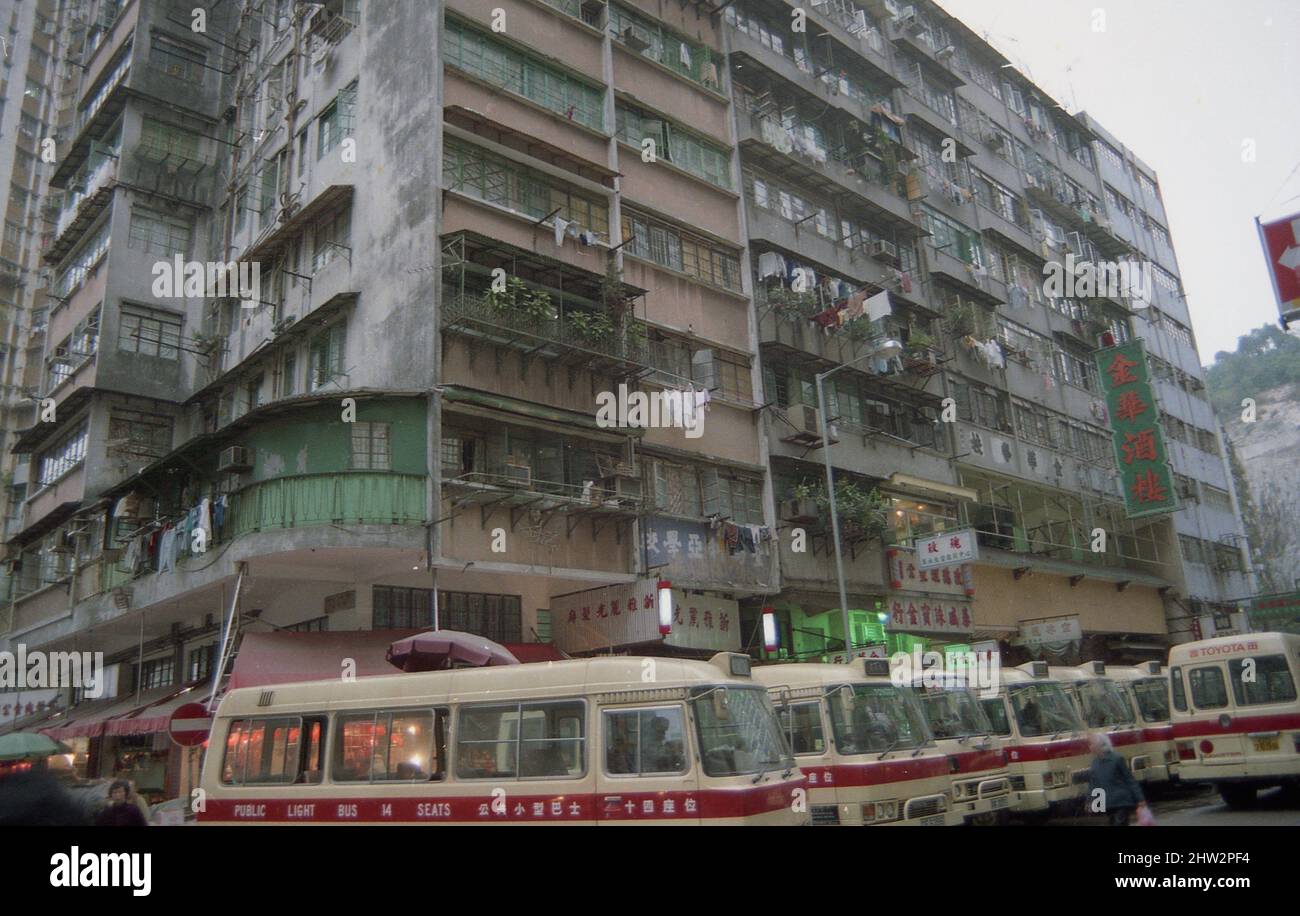 1980s, Seitenansicht vom Boden eines großen Mehrfamilienhauses im Zentrum Hongkongs, zeigt die hohe Dichte Gehäuse und dann auf der Straße, geparkt, eine Reihe der cremefarbenen öffentlichen Lichtbusse (PLBs). Diese Minibusse, ein beliebter öffentlicher Nahverkehr, tauchten erstmals 1969 auf und sind lokal als Van Jai bekannt, was van-ette bedeutet. Stockfoto