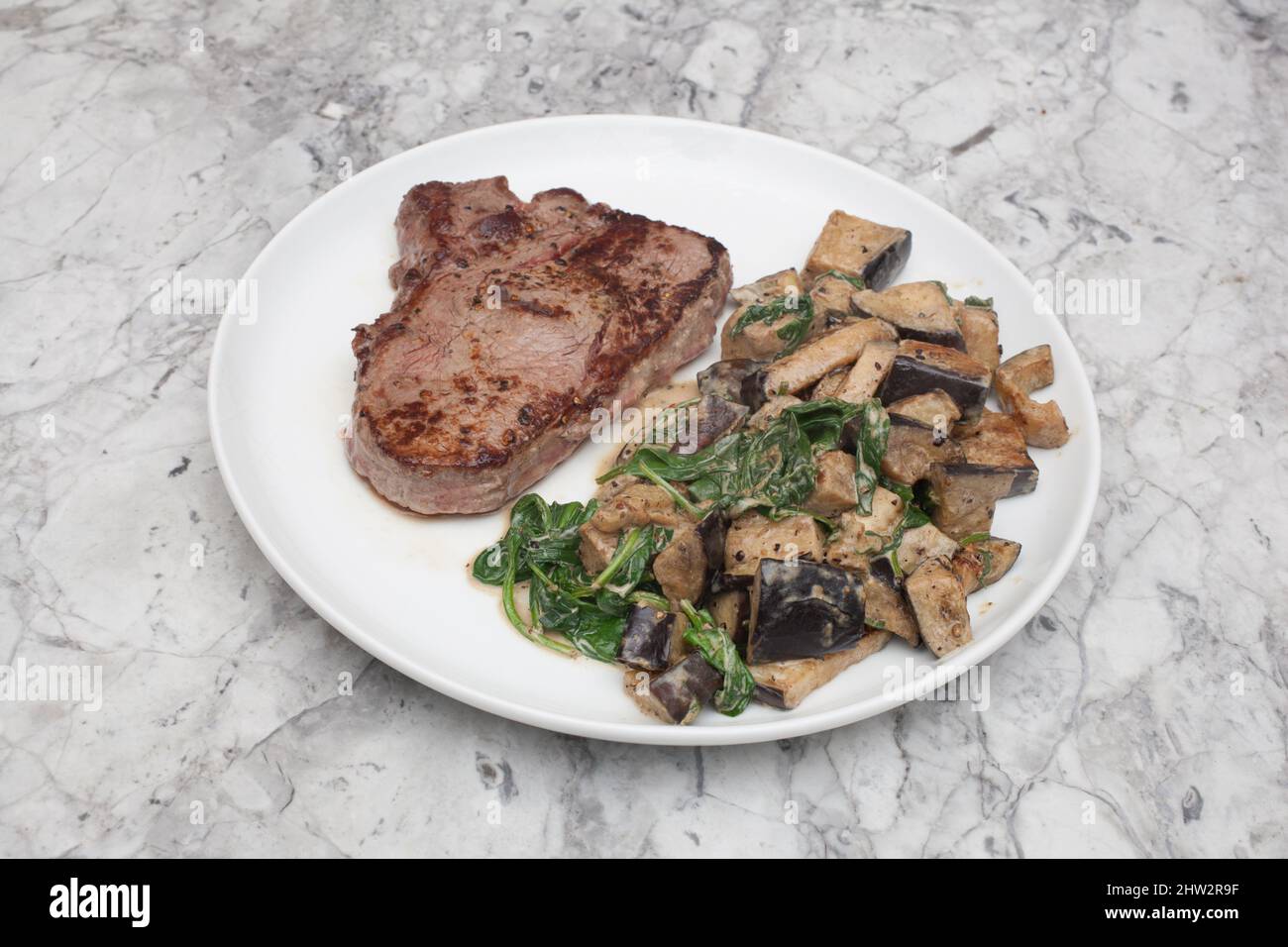 Ein Steak mit Rippenaugen, das Medium mit Auberginen und Spinat in einer cremigen Sauce zubereitet wird Stockfoto