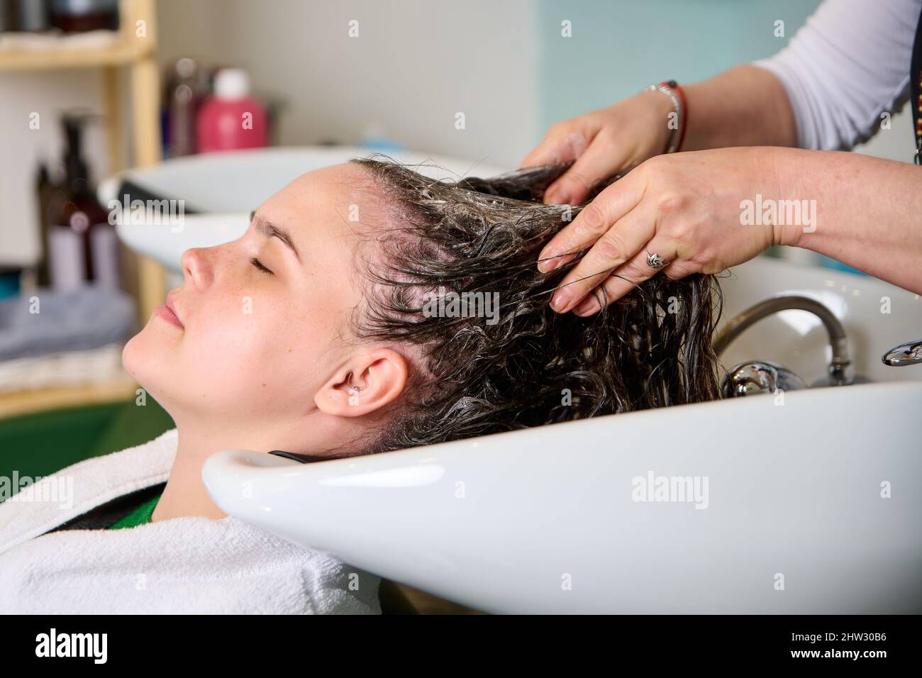 Friseur wäscht den Kopf eines brünetten Mädchens mit Shampoo im Schönheitssalon Stockfoto