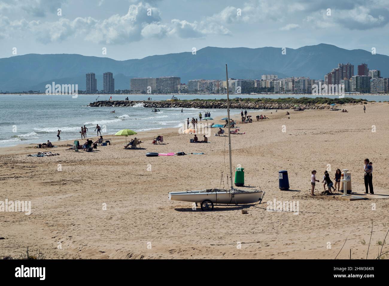 Menschen, die sich mit ihren Sonnenschirmen auf dem Sand sonnen und am Strand von Cap Blanc in der Küstenstadt Cullera in der Provinz Valencia, Spanien, baden. Stockfoto