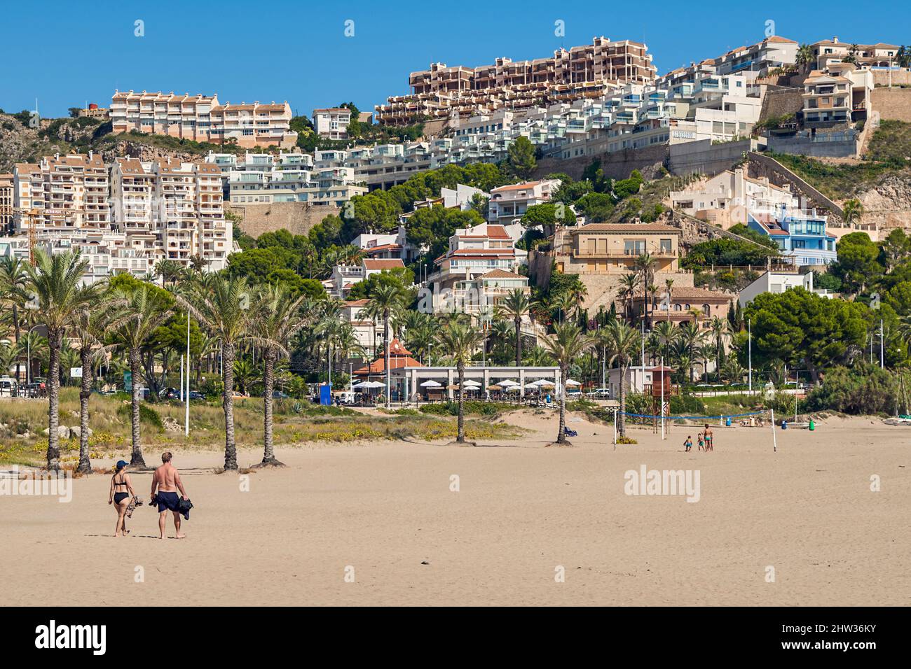 Menschen, die sich mit ihren Sonnenschirmen auf dem Sand sonnen und in der Platja de l'Illa der Küstenstadt Cullera in der Provinz Valencia, Spanien, baden, Stockfoto