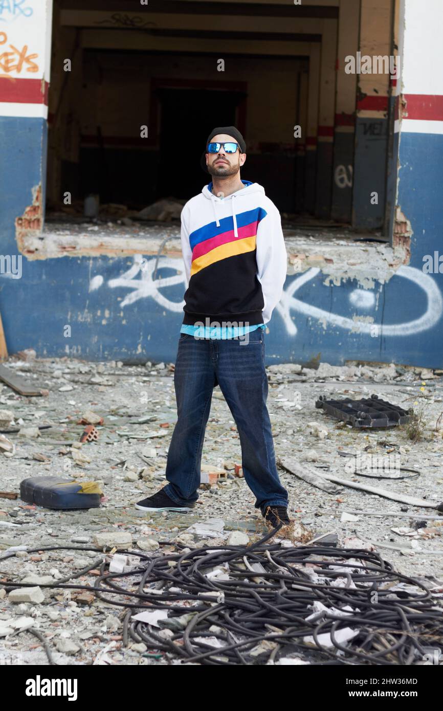 Das urbane Leben. Ein trendiger Mann, der vor einer Graffiti-Wand in einem Schrottplatz steht. Stockfoto