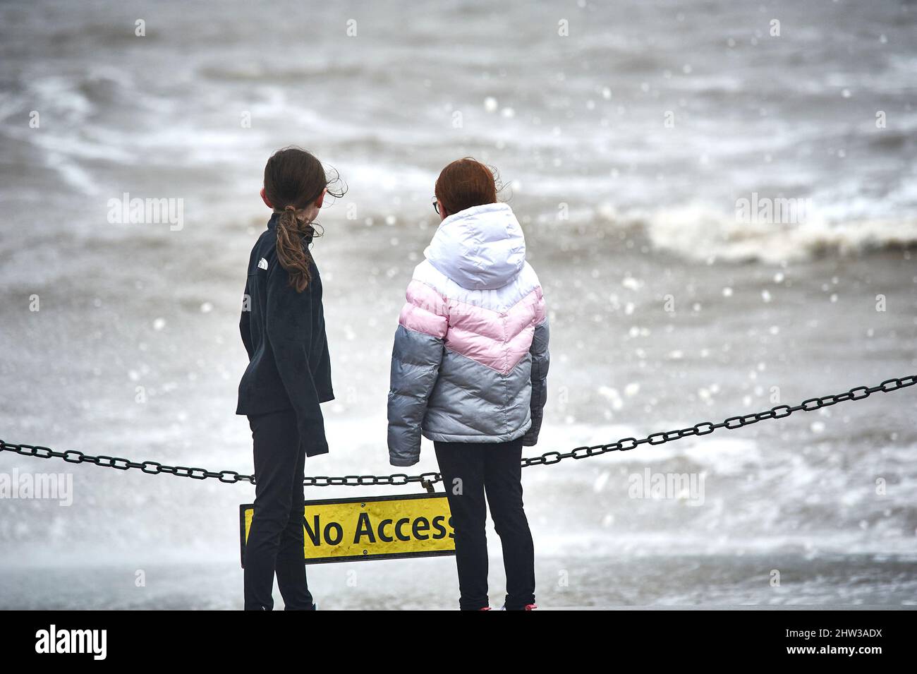 Zwei junge Mädchen beobachten ein wildes stürmisches Meer in Blackpool Stockfoto