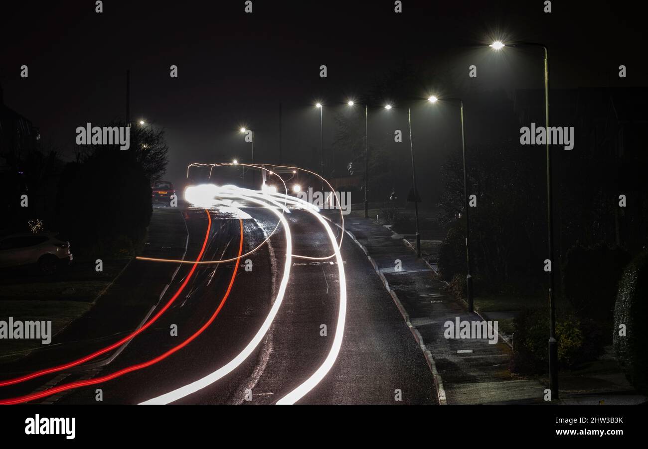 Streifen von Autoscheinwerfern und Heckleuchten, während sie nachts unter der Straßenbeleuchtung, Worcestershire, England, eine Wohnstraße entlang fahren. Stockfoto