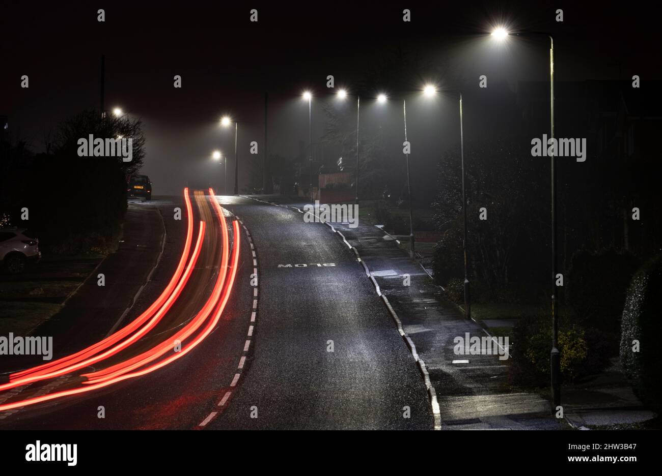 Streifen von Autoscheinwerfern und Heckleuchten, während sie nachts unter der Straßenbeleuchtung, Worcestershire, England, eine Wohnstraße entlang fahren. Stockfoto