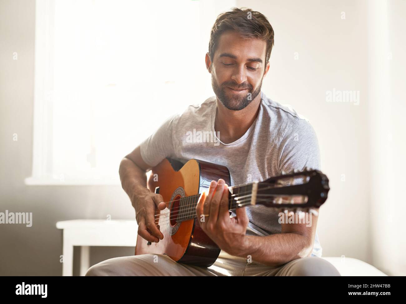 Sein musikalisches Talent zu verfeinern. Aufnahme eines hübschen jungen Mannes, der zu Hause Gitarre spielt. Stockfoto