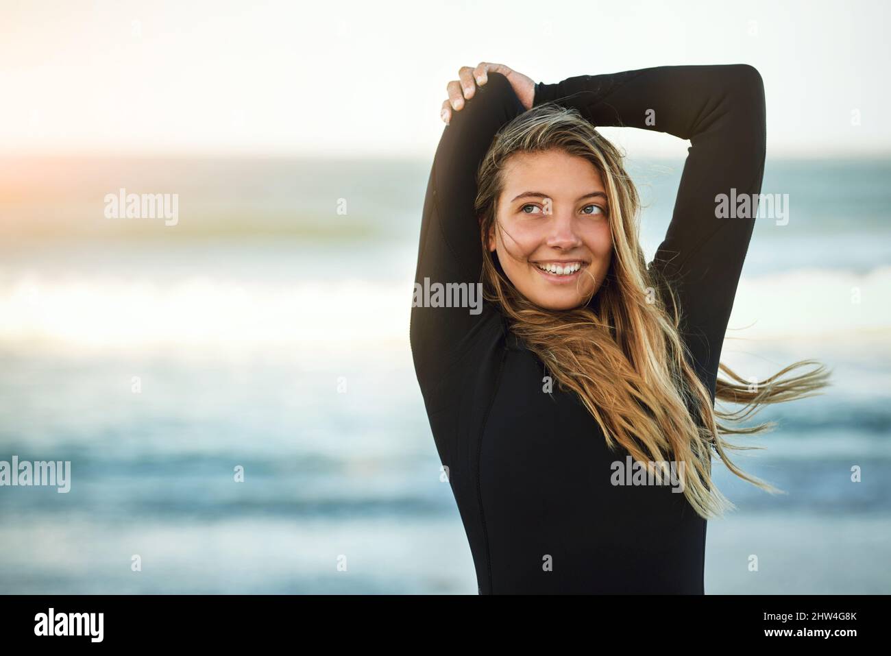 Du musst etwas licker sein, um ein Surfer zu sein. Kurzer Schuss einer attraktiven jungen Surferin, die sich am Strand aufwärmt. Stockfoto