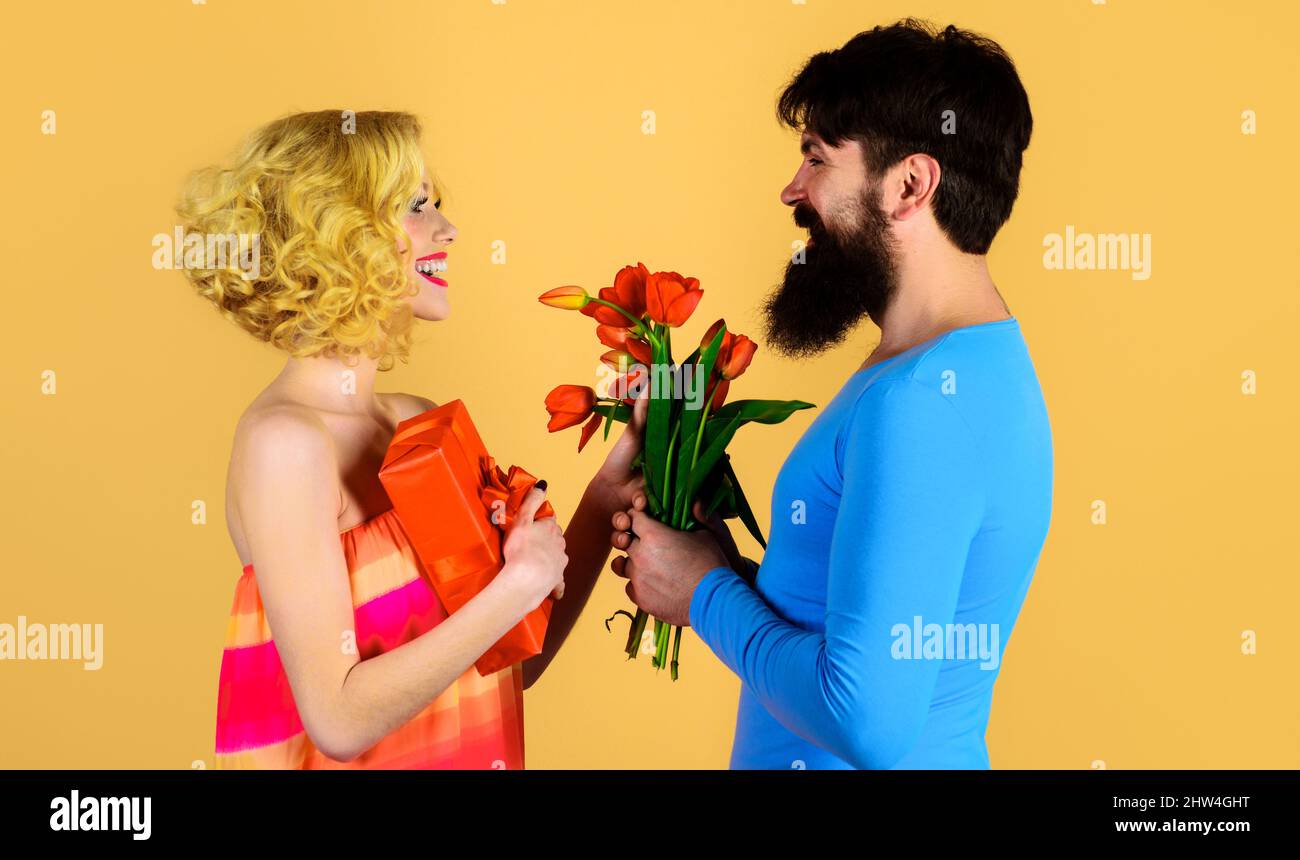 Glücklicher bärtiger Mann schenkt der Frau Blumen und Geschenke. Liebe, Beziehung. Ein Paar mit einem Blumenstrauß von Tulpen. Stockfoto