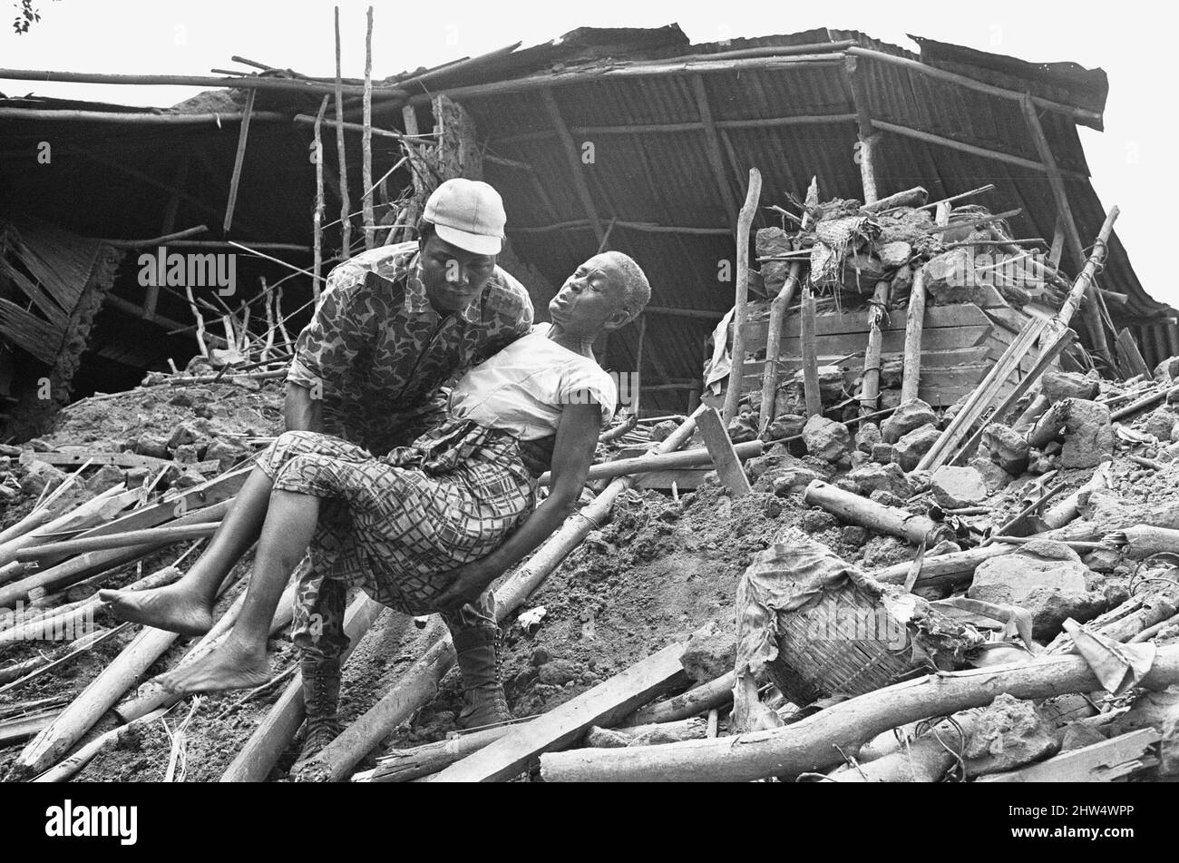 Ein biafranischer Soldat hat hier gesehen, wie er einer alten Dame aus dem Wrack ihres Hauses nach einem Artilleriebombard der nigrischen Armee half. 11.. Juni 1968The der nigerianische Bürgerkrieg, auch bekannt als Biafraner Krieg, dauerte zweieinhalb Jahre, vom 6. Juli 1967 bis zum 15. Januar 1970, und wurde gekämpft, um der Abspaltung von Biafra von Nigeria entgegenzuwirken. Die indigenen Igbo-Bewohner von Biafra fühlten sich nach der Unabhängigkeit von Großbritannien nicht mehr mit der nordeuropäischen Bundesregierung koexistieren können. Politische, wirtschaftliche, ethnische, kulturelle und religiöse Spannungen kochten schließlich in einen Bürgerkrieg über Stockfoto