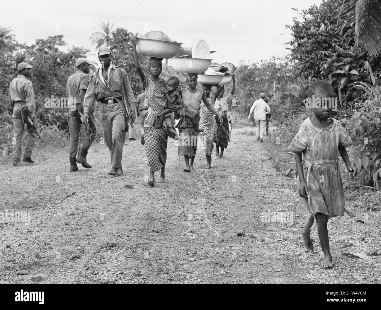 Mütter, die ihre Babys und ihren ganzen Besitz tragen, fliehen auf der Suche nach Nahrung an die Front. 5.. Juli 1968The der nigerianische Bürgerkrieg, auch bekannt als Biafraner Krieg, dauerte zweieinhalb Jahre, vom 6. Juli 1967 bis zum 15. Januar 1970, und wurde gekämpft, um der Abspaltung von Biafra von Nigeria entgegenzuwirken. Die indigenen Igbo-Bewohner von Biafra fühlten sich nach der Unabhängigkeit von Großbritannien nicht mehr mit der nordeuropäischen Bundesregierung koexistieren können. Politische, wirtschaftliche, ethnische, kulturelle und religiöse Spannungen kochten schließlich nach dem Militärputsch von 1966 in einen Bürgerkrieg über, und dann in einen Bürgerkrieg Stockfoto