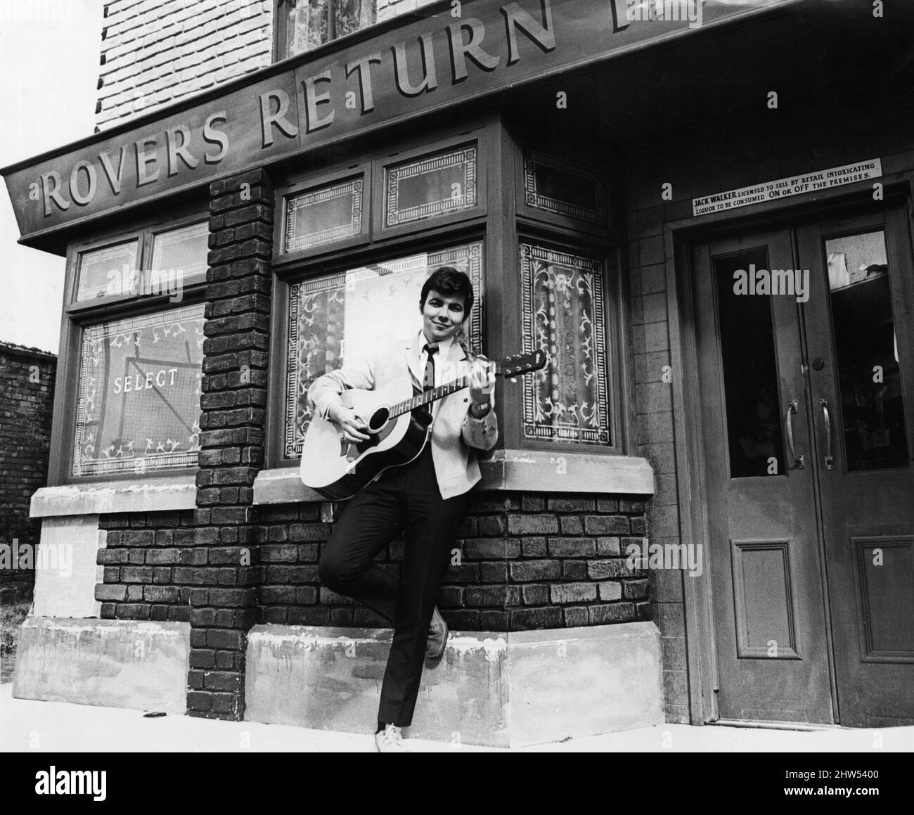 Der Schauspieler Bill Kenwright, der Gordon Clegg in der Fernsehsoap Cornation Street spielt, posiert kurz vor der Veröffentlichung seiner neuen Platte, die er im Programm singen wird, mit seiner Gitarre in der berühmten Straße. 23.. Juli 1968. Stockfoto