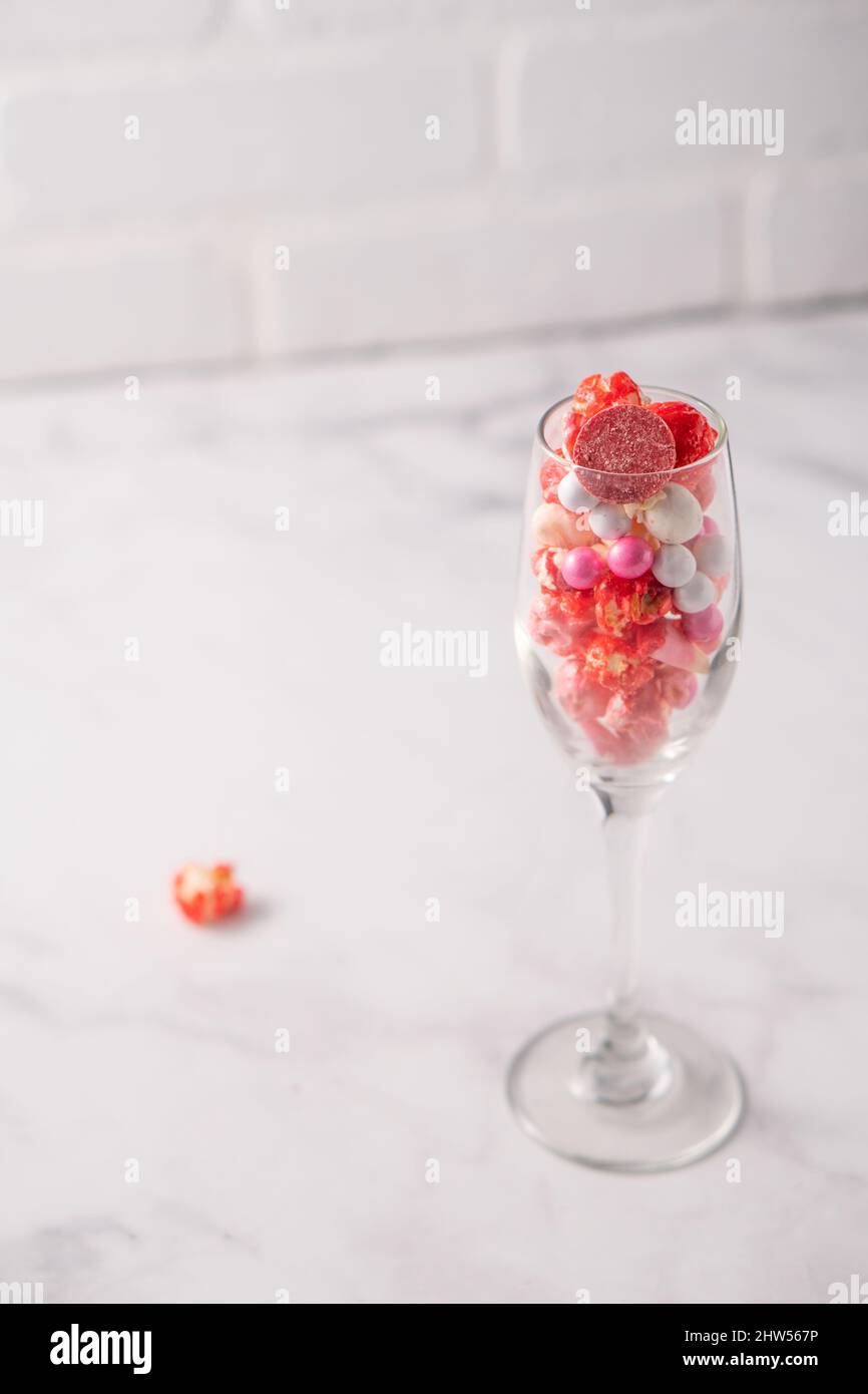 Farbenfrohe rote und rosafarbene, kandierte Popcorn mit gemischten Süßigkeiten in Sektflöte. Stockfoto