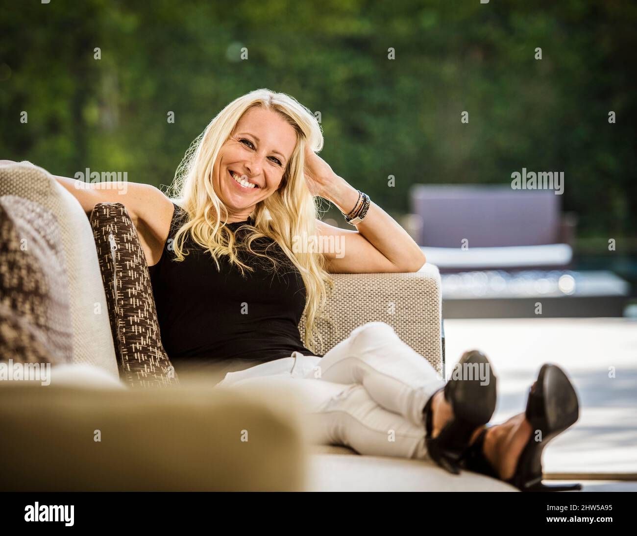 Porträt einer lächelnden blonden Frau, die auf dem Sofa sitzt Stockfoto