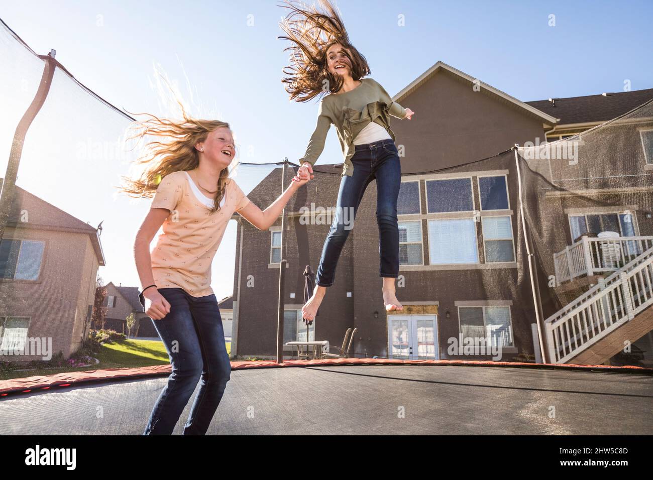 Mädchen (10-11, 12-13) springen auf dem Trampolin vor dem Haus Stockfoto
