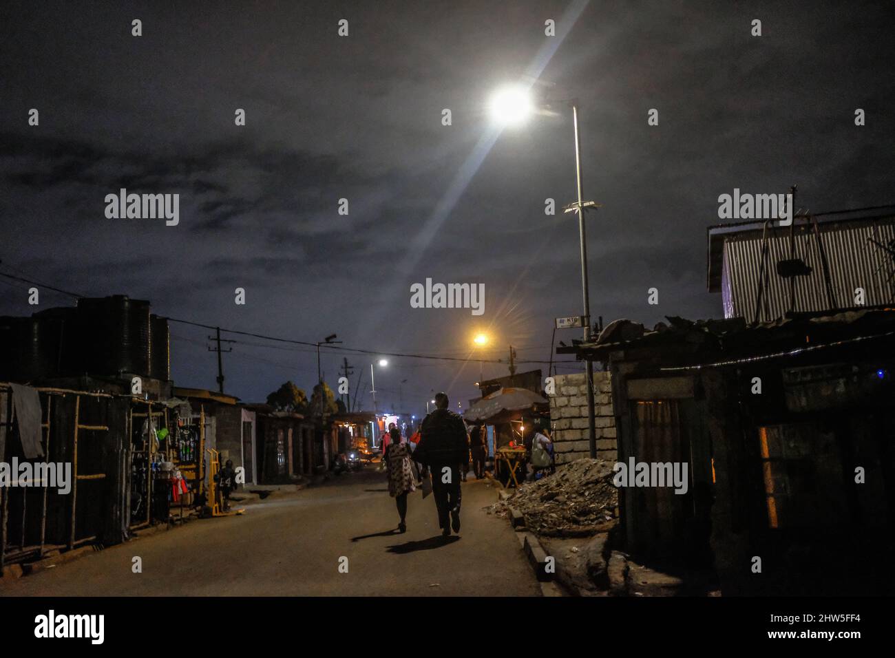 Die Anwohner gehen nach Hause zurück, vorbei an den solarbetriebenen Straßenlaternen der Gemeinde in den Slums von Kibera. Tausende von Haushalten in Kenias Slums in Kibera hängen davon ab Stockfoto