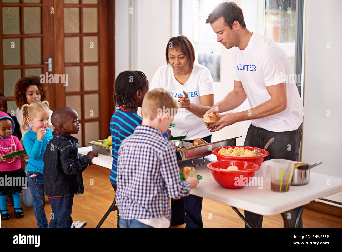 Es gibt viel für jeden. Aufnahme von Freiwilligen, die einer Gruppe von kleinen Kindern Essen servieren. Stockfoto