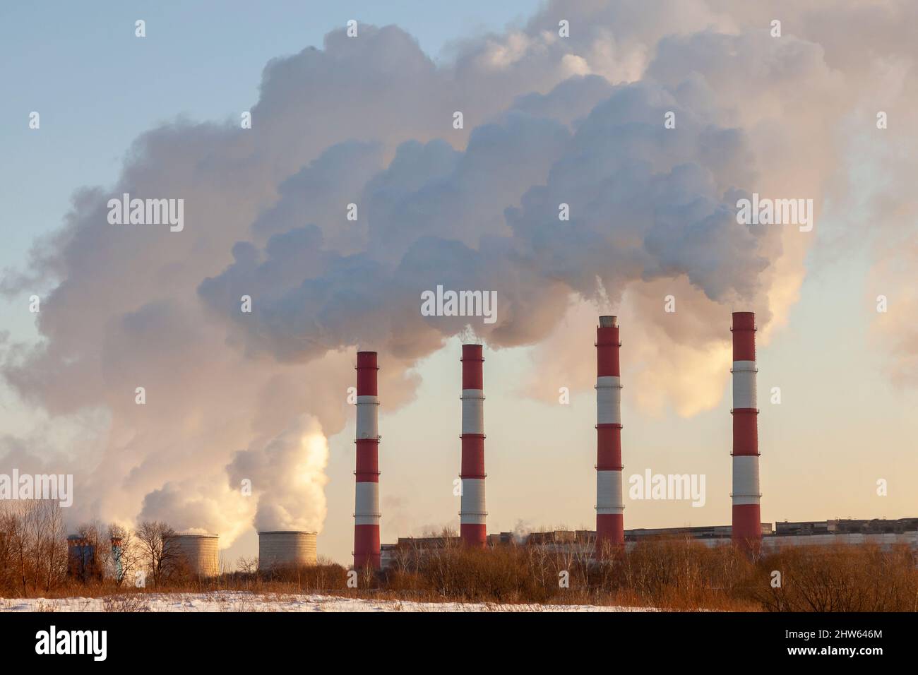 Eine Reihe von rauchenden Fabrikschornsteinen vor einem klaren Himmel. Stockfoto
