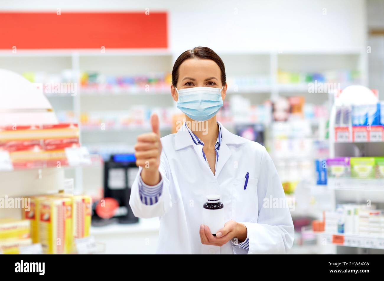 Apotheker in Maske zeigt Daumen nach oben in der Apotheke Stockfoto