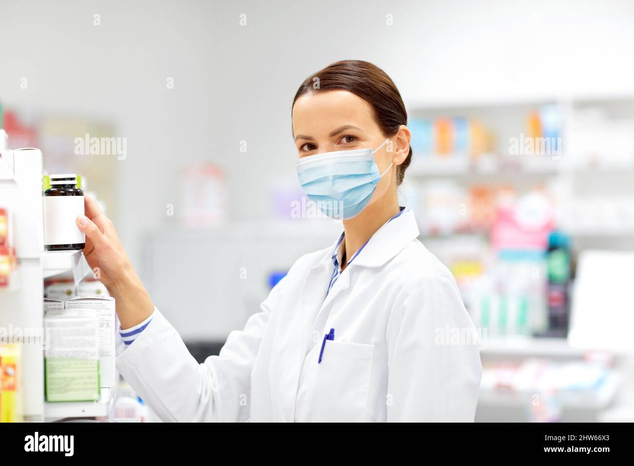 Weibliche Apotheke in Maske mit Droge in der Apotheke Stockfoto