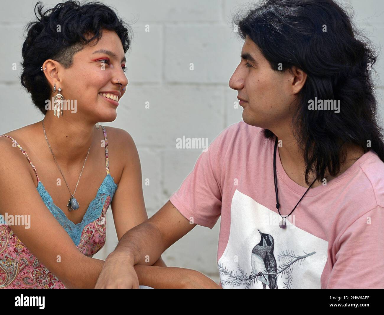 Eine schöne lächelnde junge Latina-Frau aus Mexiko und ein hübscher, ernsthafter junger Latino-Mann aus Mexiko sind verliebt und blicken einander in die Augen. Stockfoto