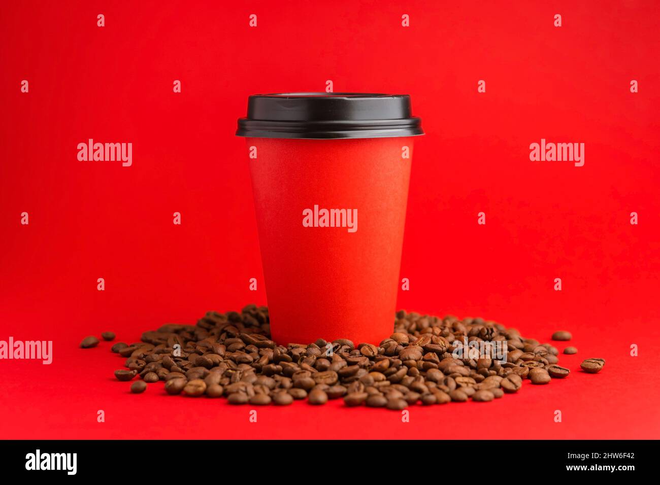 Kaffeetasse aus rotem Papier mit schwarzer Kappe stehen auf gerösteten Bohnen auf rotem Hintergrund. Modell Stockfoto