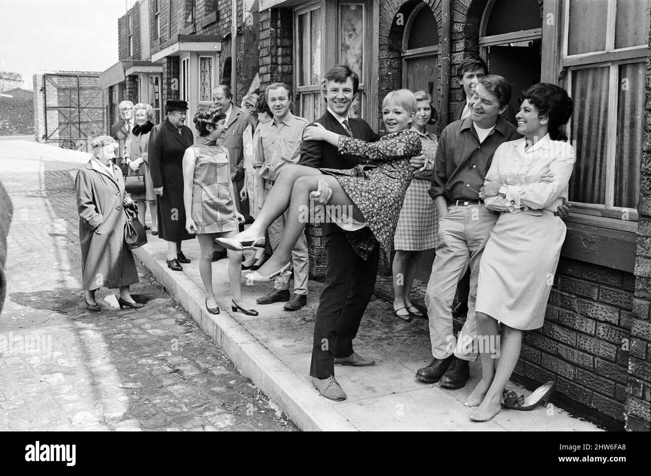 Eine neue Straßeneinstellung für die „Coronation Street“. Granada TV hat ein Outdoor-Set für einige der Szenen gebaut. Im Bild sind die Darsteller Dennis Tanner (Philip Lowrie) mit seiner Braut Jenny Sutton (Mitzi Rogers) nach ihrer Hochzeit mit Annie Walker (Doris Speed), Ena Sharples (Violet Carson), Emily Nugent (Eileen Derbyshire), Valerie Barlow (Anne Reid), Ken Barlow (William Roache) Len Fairclough (Peter Adamson) und Elsie Tanner (Pat Phoenix). 18. Mai 1968. Stockfoto