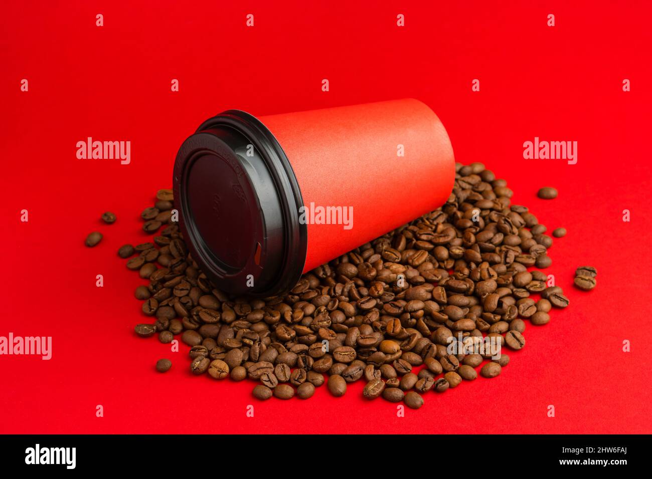 Kaffeetasse aus rotem Papier mit schwarzer Kappe liegen auf gerösteten Bohnen auf rotem Hintergrund. Modell Stockfoto