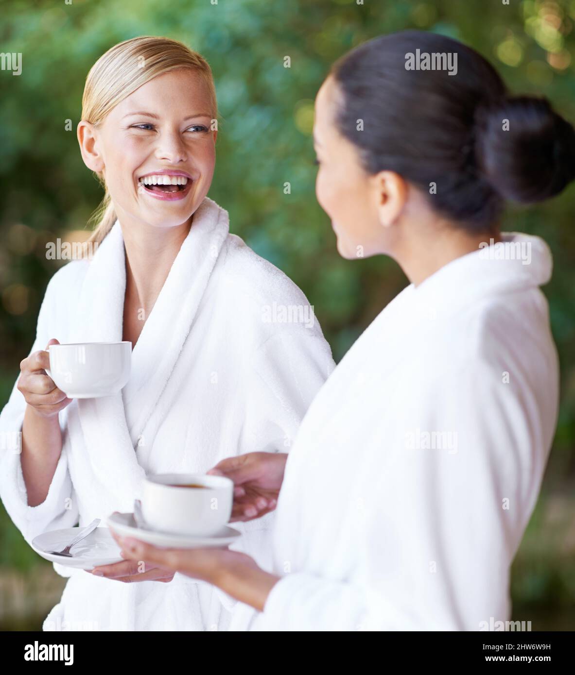 Genießen Sie eine Verwöhnstunde mit einem guten Freund. Zwei junge Frauen, die Kaffee in ihren Bademänteln im Spa trinken. Stockfoto