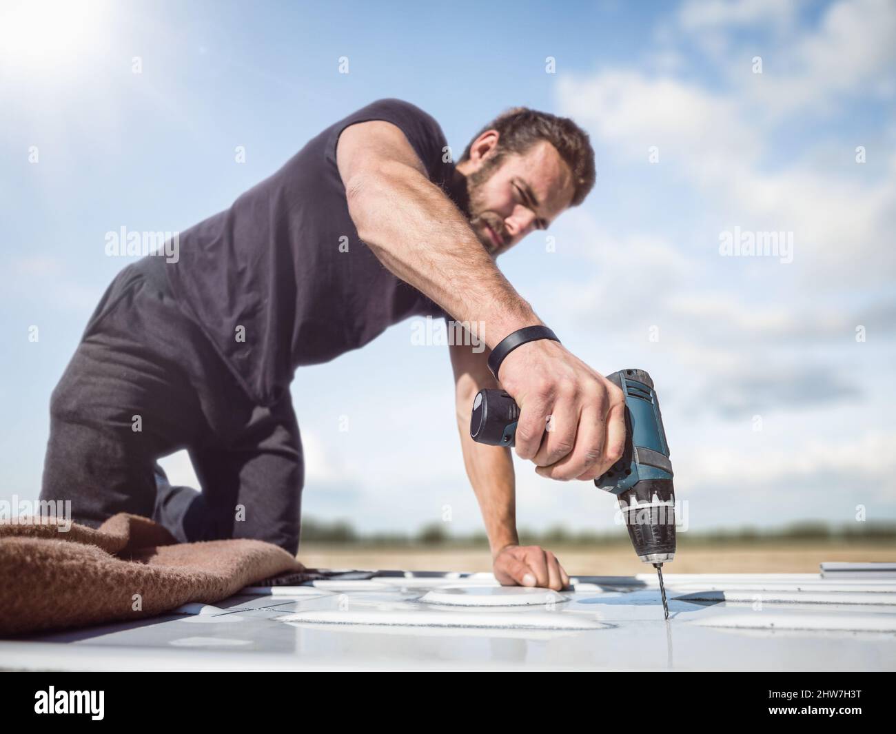 Mann, der mit einem Akku-Bohrschrauber auf dem Dach eines Transporters arbeitet Stockfoto
