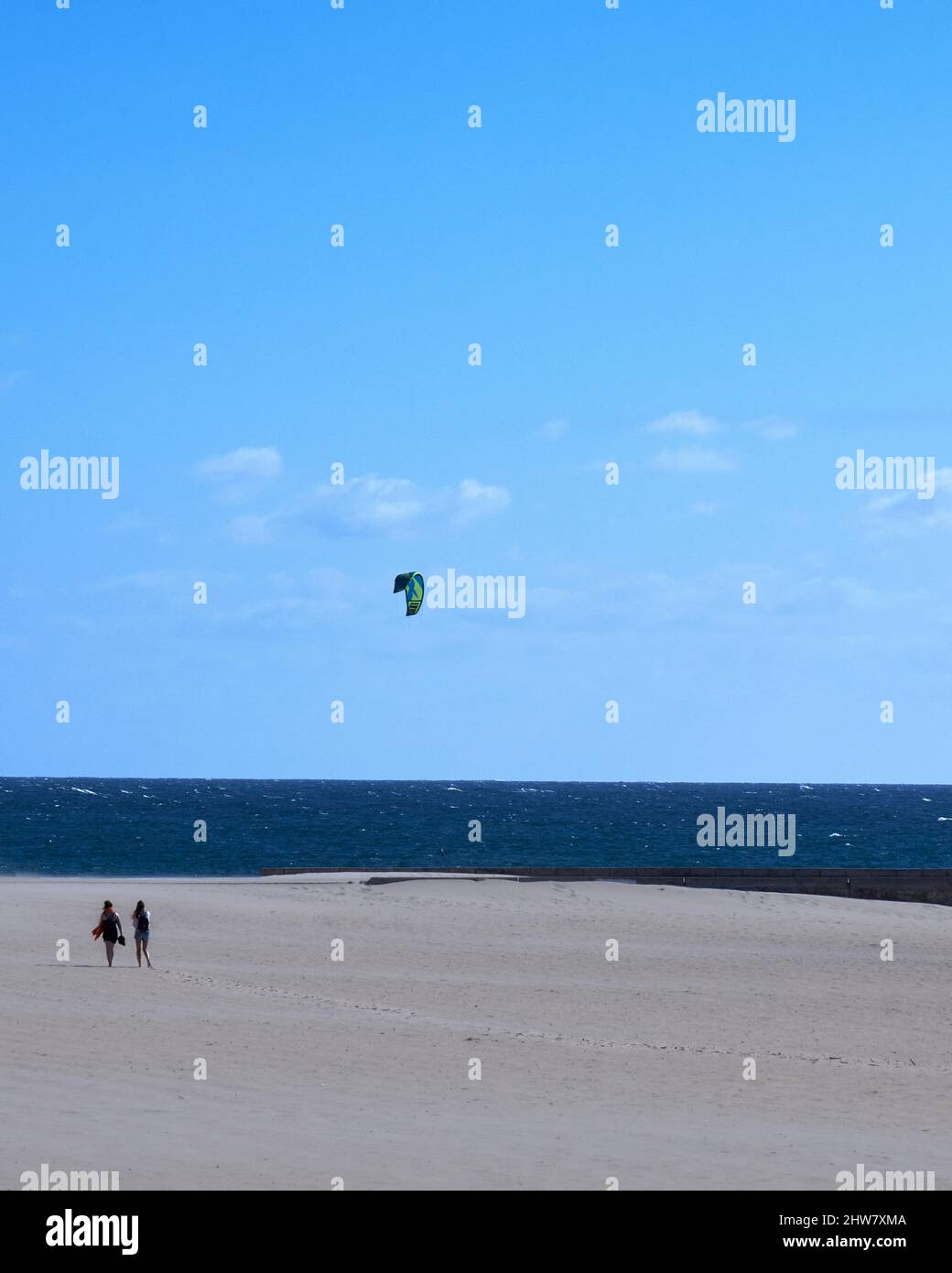 Senkrecht von zwei Personen, die am sandigen Barra-Strand gegen die Kitesurfer in der blauen Meereslandschaft wandern Stockfoto