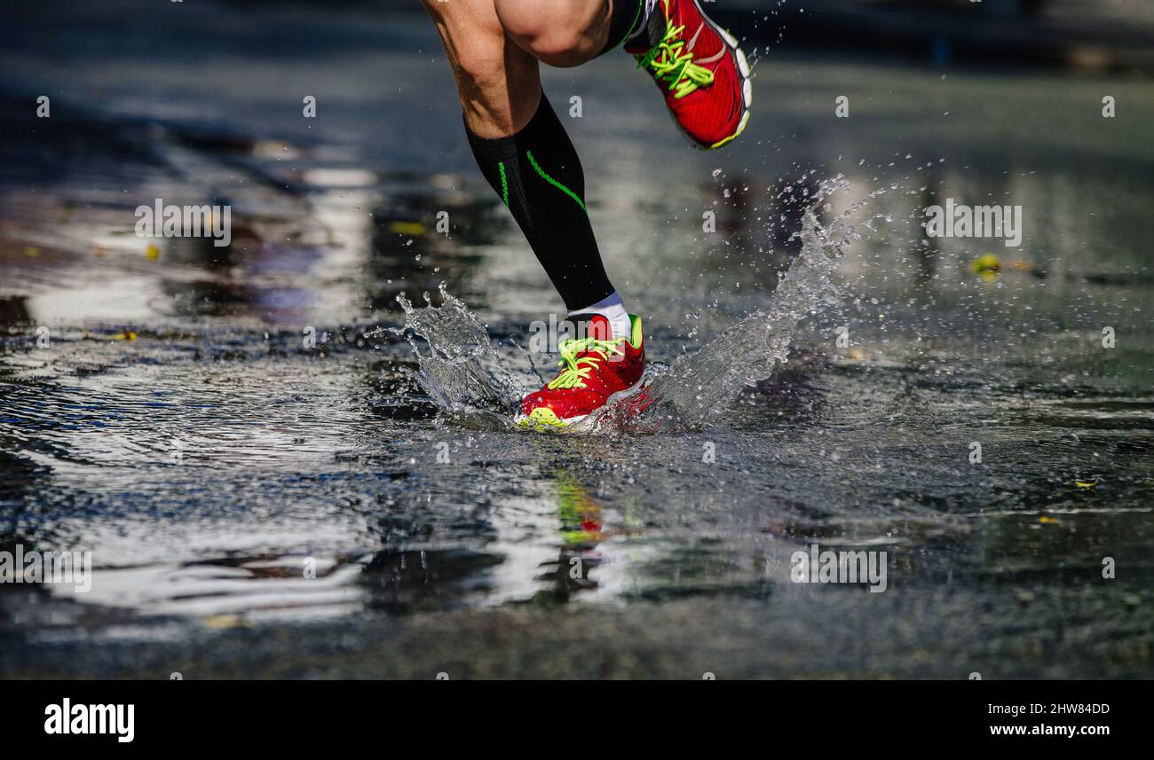 Die Beine der Läufer in Kompressionssocken laufen in einer Pfütze, die Wasser spritzt Stockfoto