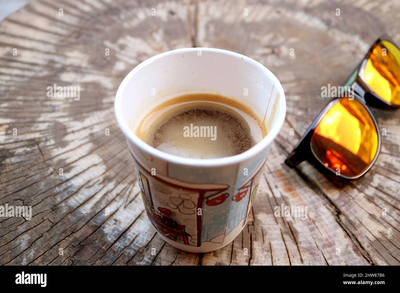 Heißer Kaffee in einer Papiertasse auf einem Baumstumptisch mit Sonnenbrille Stockfoto
