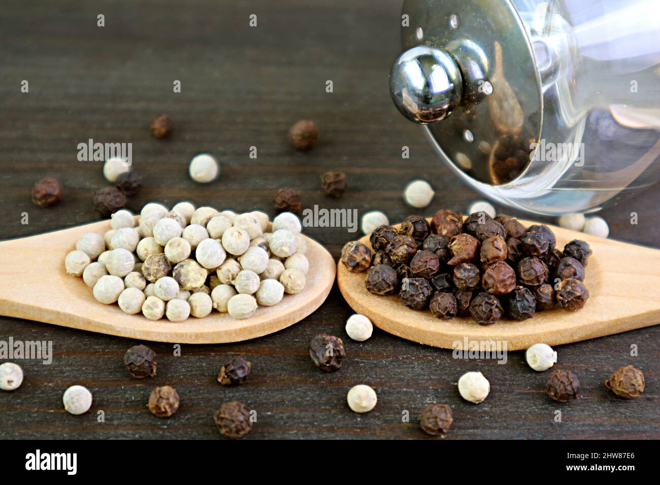 Nahaufnahme Löffel von weißen und schwarzen Pfefferkörnern mit einem Grinder auf Holzkulisse Stockfoto
