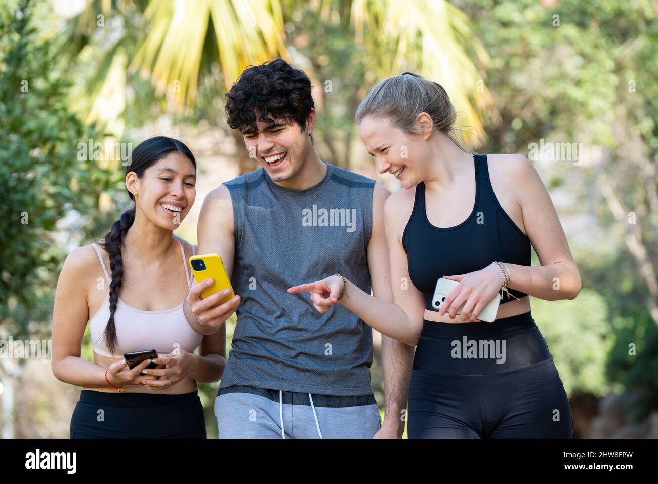 Drei junge Sportbegeisterte schauen ins Telefon und lachen im Park Stockfoto