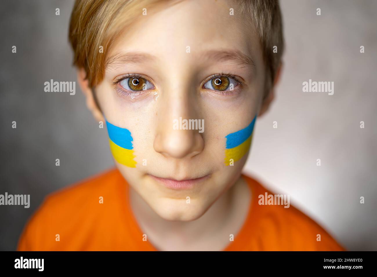 Ein trauriges Kind gegen den Krieg, ein Junge mit Tränen in den Augen und einer bemalten Flagge der Ukraine auf seinen Wangen blickt mit Mitleid auf die Kamera Stockfoto