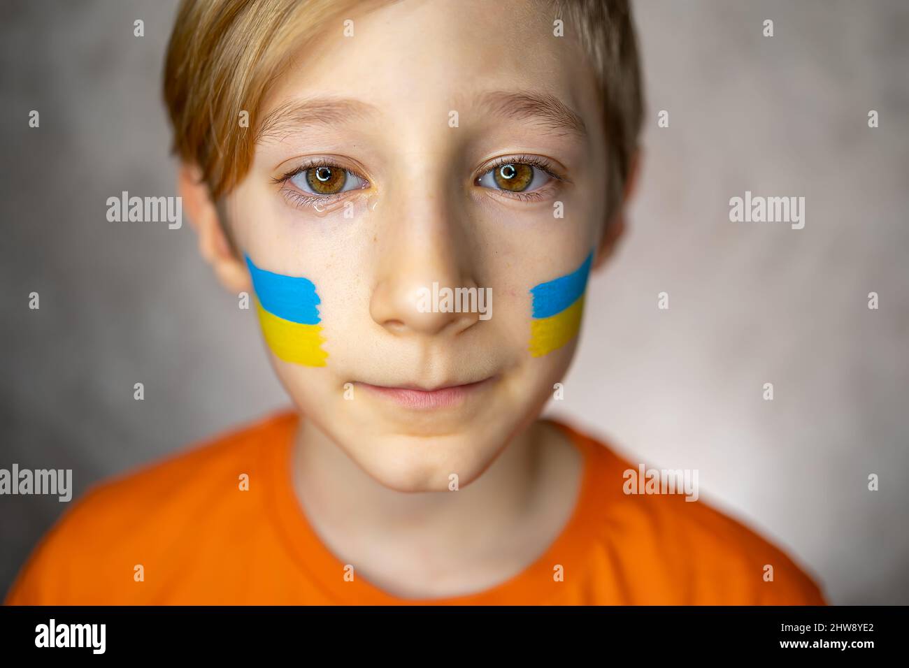 Ein trauriges Kind gegen den Krieg, ein Junge mit Tränen in den Augen und einer bemalten Flagge der Ukraine auf seinen Wangen blickt mit Mitleid auf die Kamera Stockfoto