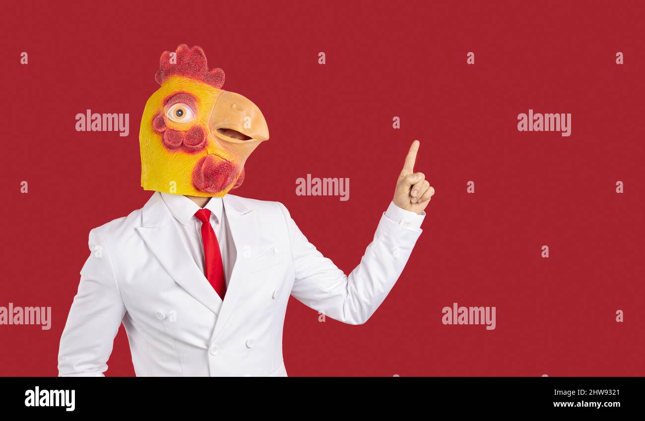 Verrückter Kerl in Anzug und Hühnermaske zeigt Finger zur Seite auf roten Kopie Raum Hintergrund Stockfoto