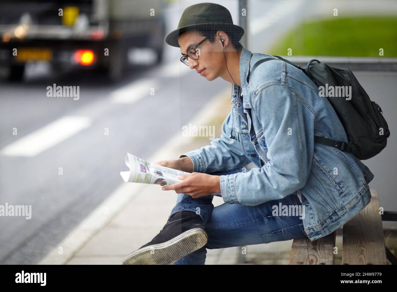 Wählen einer Route. Hip, junger Mann, der an einer Bushaltestelle sitzt, während er sich eine Karte anschaut. Stockfoto