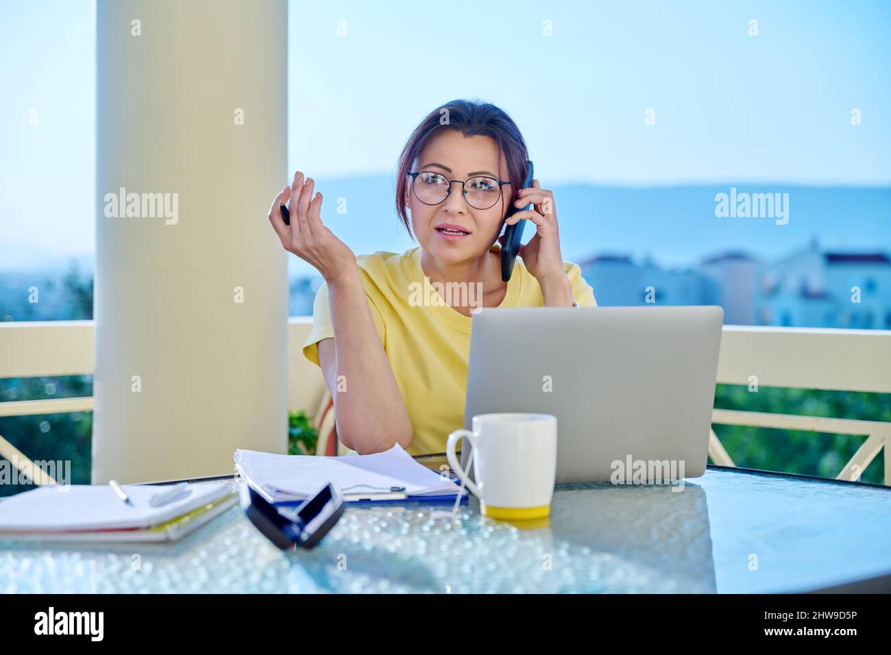 Frau mittleren Alters, die im Heimbüro auf der Terrasse arbeitet und telefoniert Stockfoto