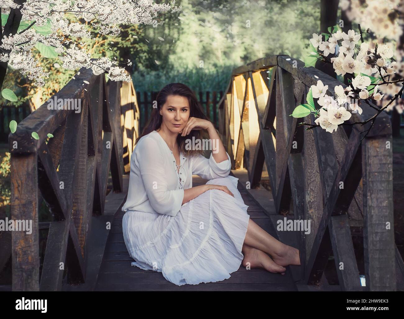 Frau in weißen Kleidern sitzt auf einer Brücke in einem schönen Feenplatz Stockfoto
