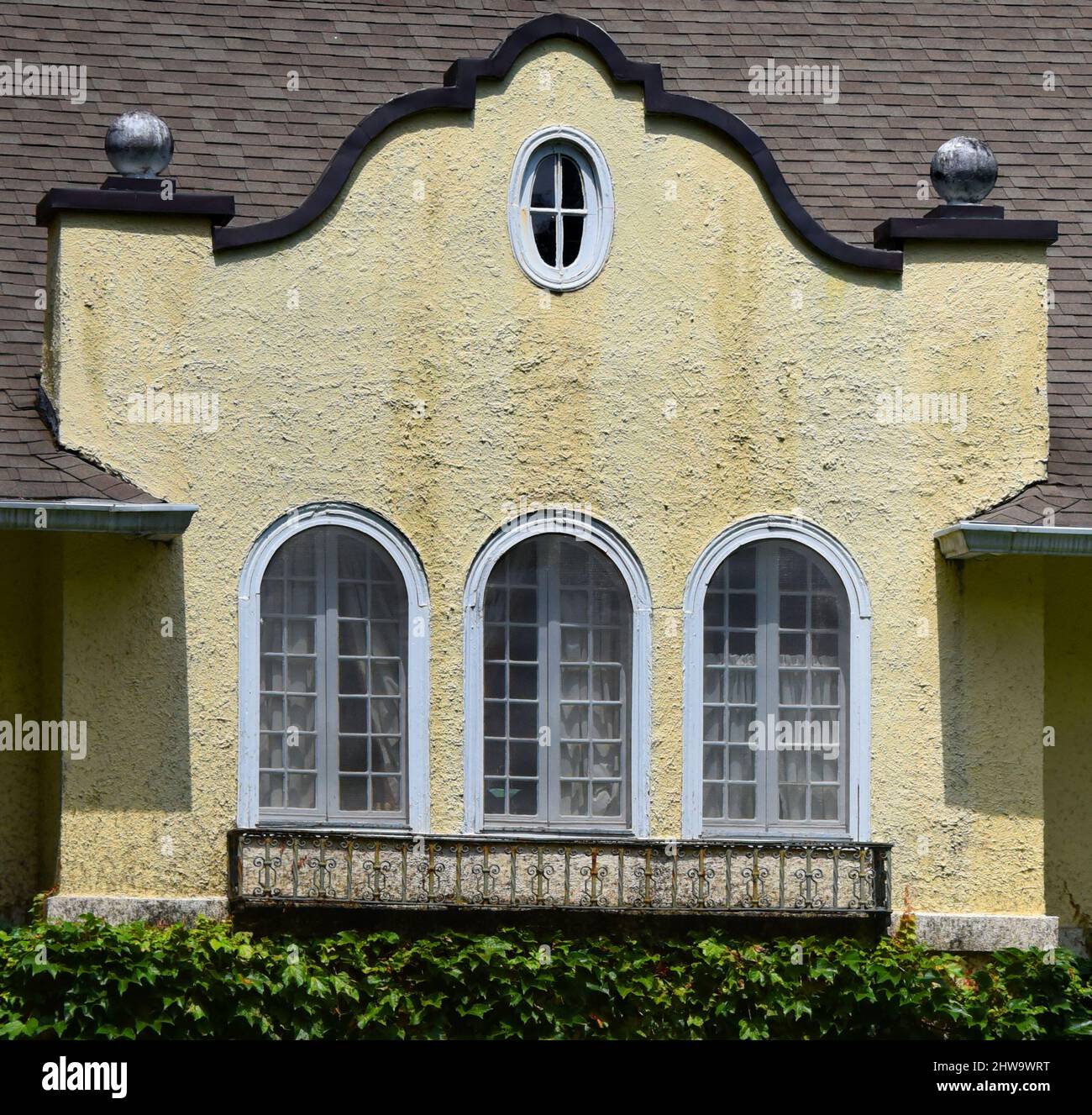 Die gelb getönten Stuckfenster haben gewölbte und runde Fenster. Kleiner dekorativer Balkon unter den Fenstern. Stockfoto