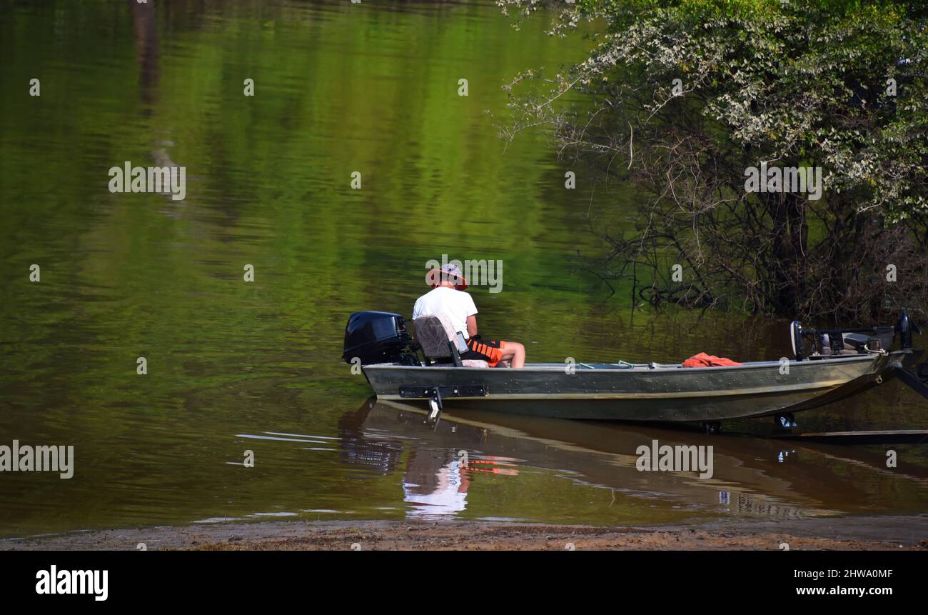 Der Mensch bereitet sein Boot vor, während er sich auf einen Tag beim Angeln auf dem Ouachita River in Arkansas vorbereitet. Er hat Shorts und einen Hut, beide mit Orange getrimmt. Stockfoto